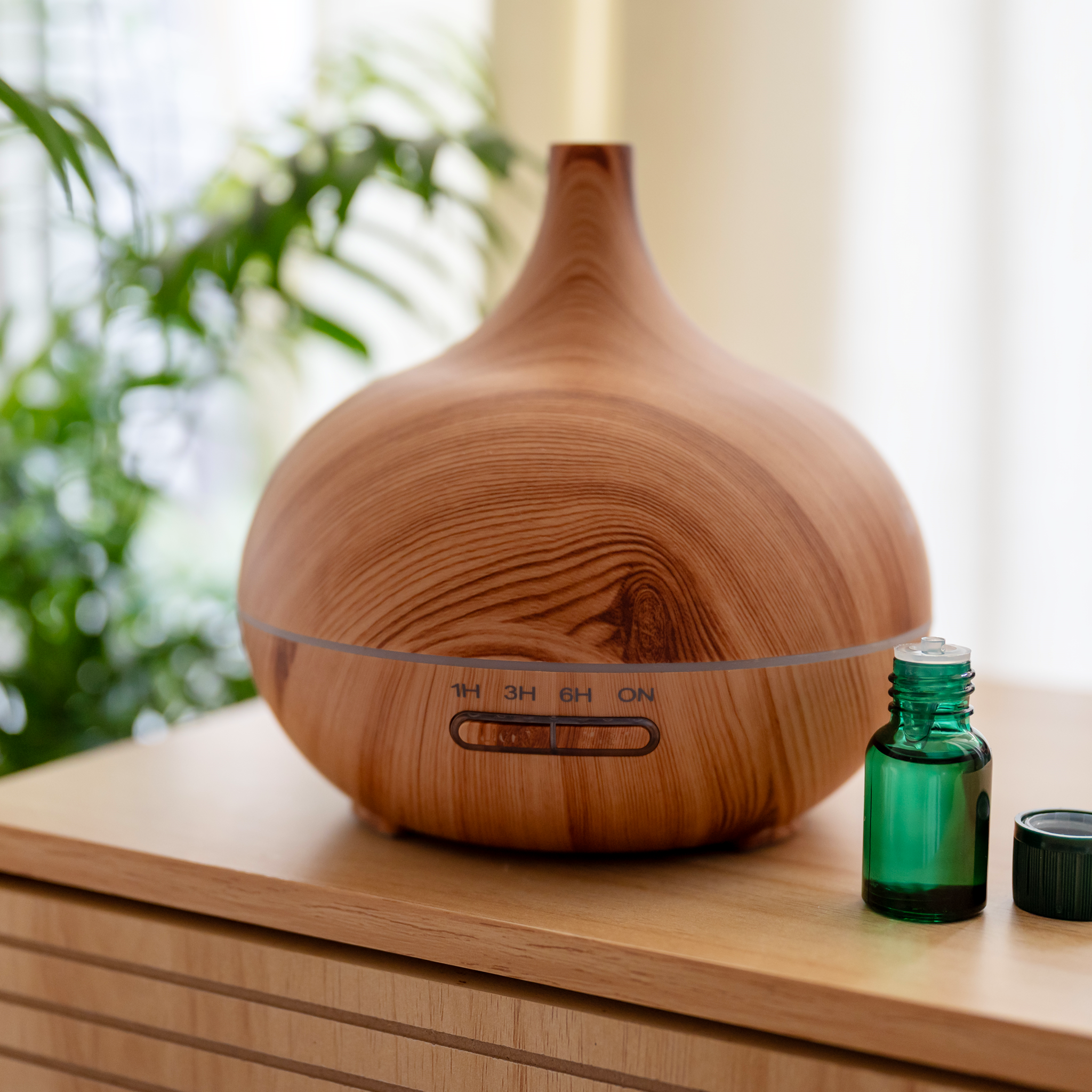 Elegant raindrop-shaped wood grain aromatherapy diffuser alongside a bottle of pure essential oil on a clean surface.